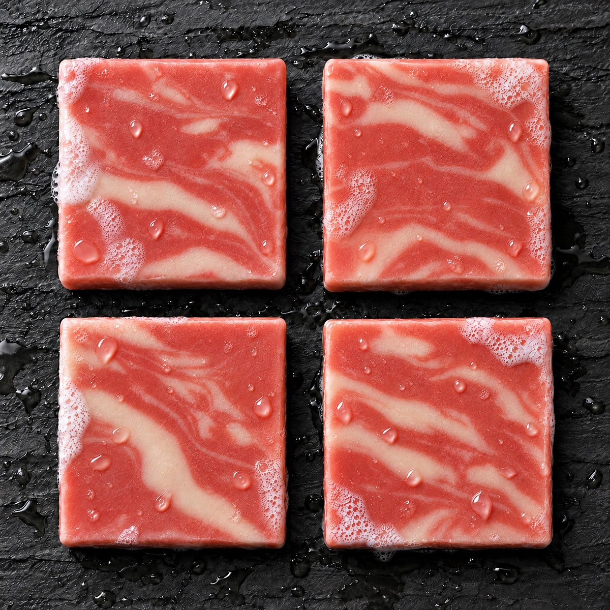 Overhead view of four Honor and Sacrifice red and cream marbled soap bars on wet slate
